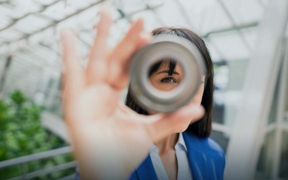 Kiesow Oberflächenchemie Frau schaut mit einem Auge durch ein metallenes rundes Objekt
